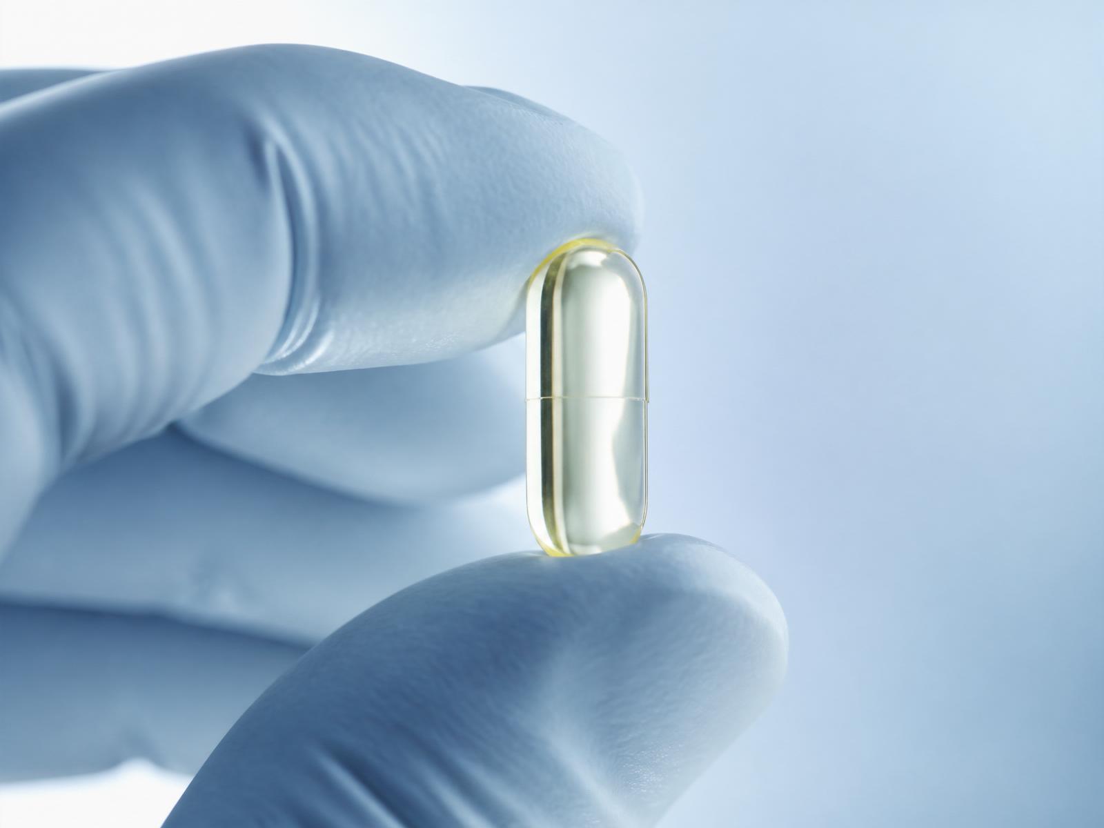 Gloved clinician hand holding a translucent supplement capsule under soft ice-blue clinical light